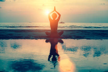 Silhouette yoga woman on the sea beach at sunset.の写真素材