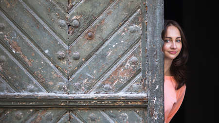 Young woman peeks out from behind big ancient doors.の写真素材