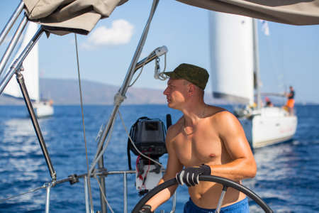 Man at the helm controls of a sailing boat during sea yacht race.