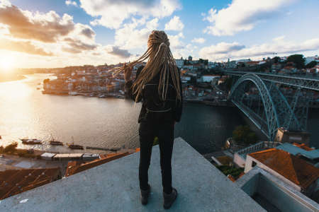 Girl with blonde dreadlocks standing on the background of the bridge Dom Luis I over Douro river, Porto, Portugal.の写真素材