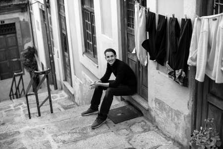 Young fashionable guy on the streets of a European town, sitting on the porch of the house. Black-and-white photo.の写真素材