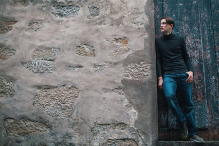 Handsome young man standing near old stone wall. Picture with space for text.