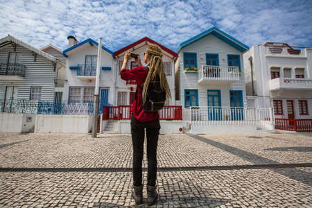 Traveller girl with blonde dreadlocks is takes photo on a smartphone striped houses in Costa Nova, Portugalの写真素材