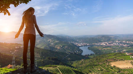 Young woman standing on the edge of a cliff looking at the Douro Valley. Vineyards are on a hills, Portugal.の写真素材