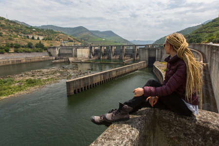Young woman sitting near an old hydroelectric plantの写真素材