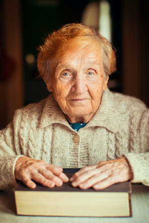 Elderly woman portrait with book sitting at table.の写真素材