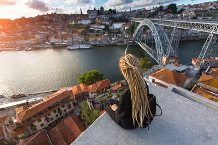 Young beautiful woman with blond dreadlocks meets sunset on the viewing platform opposite the Dom Luis I bridge across the Douro river in Porto, Portugal.の写真素材