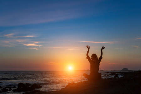 Silhouette of young Yoga woman doing exercises on the sea beach during sunset.の写真素材