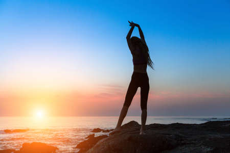 Silhouette of dancing young slim woman on the ocean coast during an amazing sunset.の写真素材