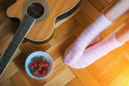 On the parquet floor guitar, a ?up of strawberries, female feet in pink socks.