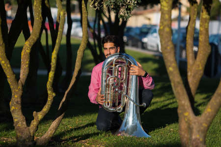 Musician with the tuba sitting on the grass in the Park.の写真素材