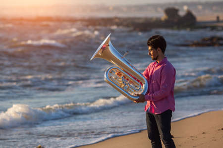 Young man with trumpet on the sea coast during surf. Tuba instrument.