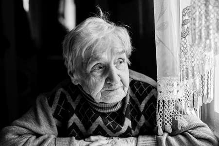 Elderly woman portrait looking out the window. Black-and-white photo of high contrast.の写真素材