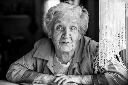An elderly woman sitting at table in the house. Emotional black and white portraits.の写真素材