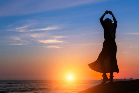 Silhouette of dancing woman on the sea coast during amazing sunset.の写真素材