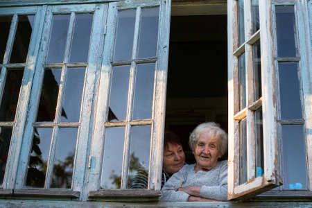 An elderly woman and her adult daughter looking out the window of the veranda.