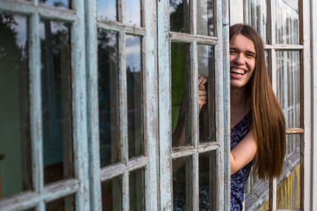 Young beautiful long-haired woman sitting on the window, summer veranda.の写真素材