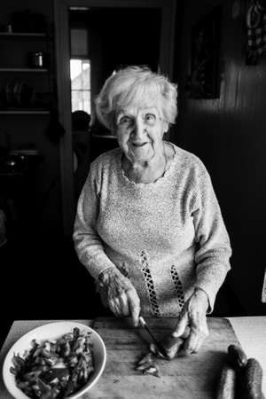 An elderly woman in the kitchen chops vegetables for salad. Black and white photo.の写真素材