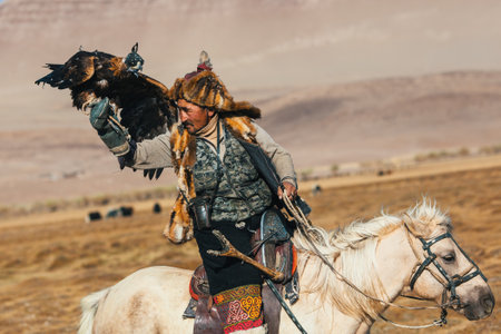 SAGSAY, MONGOLIA - SEP 28, 2017: Kazakh Eagle Hunter traditional clothing, while hunting to the hare holding a golden eagle on his arm in desert mountain of Western Mongolia.のeditorial素材