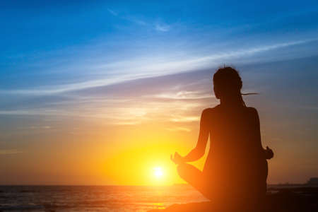 Yoga woman silhouette meditation at the sea beach during amazing sunset.の写真素材