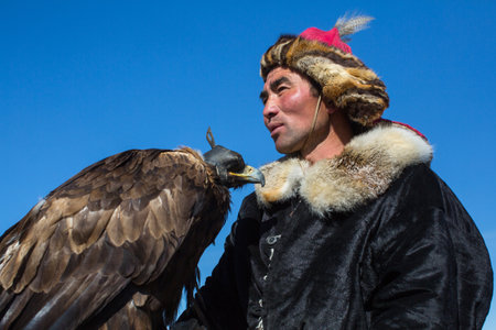 BAYAN-ULGII, MONGOLIA - SEP 30, 2017: Kazakh Eagle Hunter traditional clothing, while hunting to the hare holding a golden eagle on his arm in desert mountain of Western Mongolia.のeditorial素材