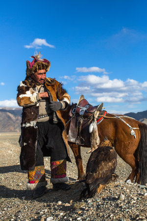 BAYAN-ULGIY, MONGOLIA - SEP 27, 2017: Kazakh Eagle Hunter at traditional clothing, on horseback while hunting to the hare holding a golden eagle on his arm in desert mountain of Western Mongolia.のeditorial素材