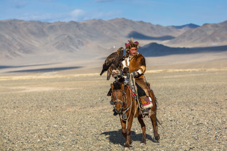BAYAN-ULGIY, MONGOLIA - SEP 27, 2017: Kazakh Eagle Hunter at traditional clothing, on horseback while hunting to the hare holding a golden eagle on his arm in desert mountain of Western Mongolia.のeditorial素材
