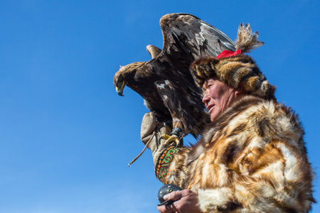 BAYAN-ULGII, MONGOLIA - SEP 30, 2017: Kazakh Eagle Hunter traditional clothing, while hunting to the hare holding a golden eagle on his arm in desert mountain of Western Mongolia.のeditorial素材