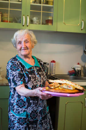 Elderly woman in the kitchen with a pie in his hands.の写真素材