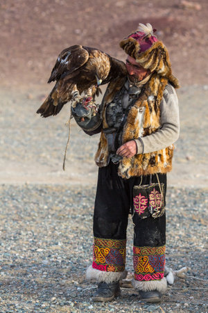 SAGSAY, MONGOLIA - SEP 28, 2017: Golden Eagle Hunter, while hunting to the hare holding a golden...