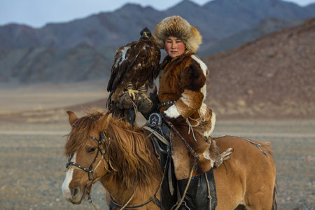 SAGSAY, MONGOLIA - SEP 28, 2017: Young woman Eagle Hunter at traditional clothing, while hunting to the hare holding a golden eagles on his arms in desert mountain of Western Mongolia.のeditorial素材
