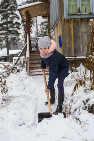 Little cute girl cleans snow to shovel near the country house.の写真素材