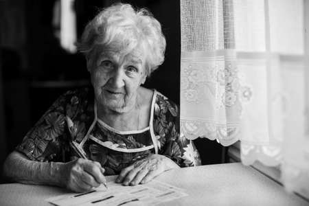 An elderly woman fills a receipt for payment of utility bills.の写真素材