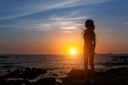 Silhouette of flexible girl with dreadlocks on ocean coast during amazing sunset.の写真素材
