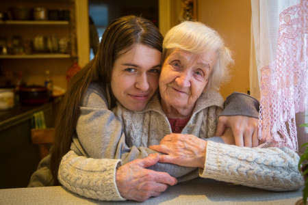An elderly woman in an embrace with an adult granddaughter posing for the camera in a village house.の写真素材