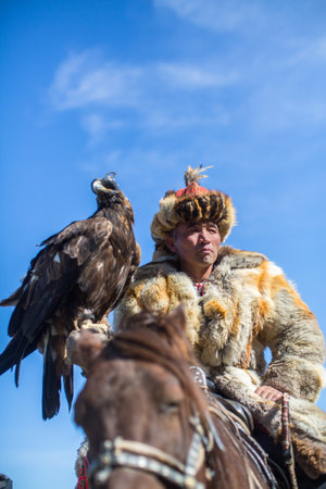 BAYAN-ULGII, MONGOLIA - SEP 30, 2017: Kazakh Eagle Hunter traditional clothing, while hunting to the hare holding a golden eagle on his arm in desert mountain of Western Mongolia.のeditorial素材