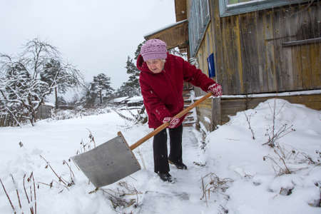Elderly woman cleans the snow near his rural home.の写真素材