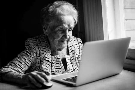 An elderly woman works on a laptop. Black-and-white photograph.の写真素材