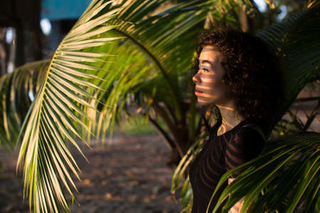 Beautiful asian girl looks through the palm leaves.の写真素材
