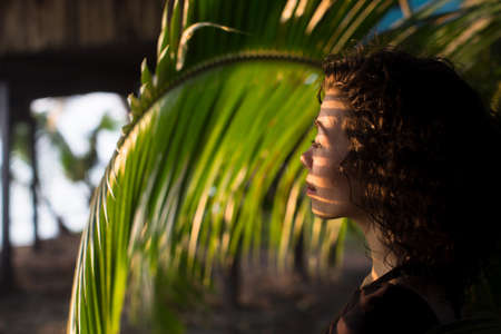 A beautiful girl looks through the palm leaves.の写真素材