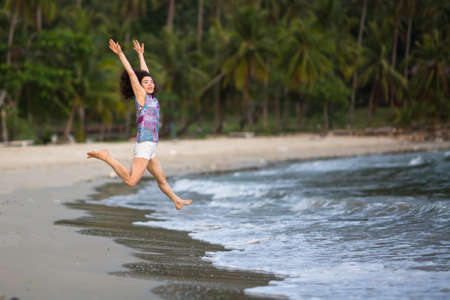 Young woman runs jumps into the sea on a tropical beach.
