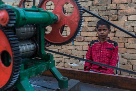 VARANASI, INDIA - MAR 14, 2018: Unidentified indian child seller of cane juice sits near the juicer...