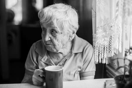 Elderly woman in the kitchen with a cup of coffee. Image in black and whiteの写真素材