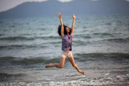 Young mixed race woman jumps on the sea beach.