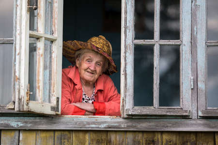 Elderly woman looking from the window of the farmhouse.の写真素材