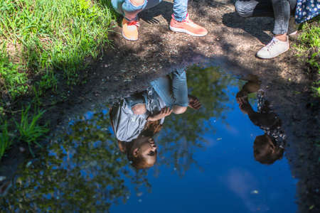 A reflection in a puddle - two sisters girls teenagers talking to each other in the Park.