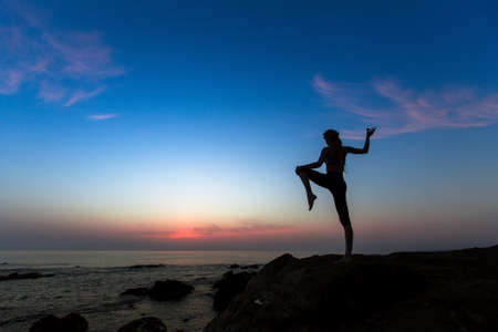 Silhouette of young woman doing gymnastics exercises on the sea shore during amazing sunset.の写真素材