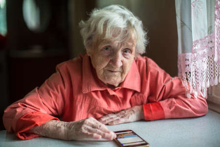 Elderly woman sits with a smartphone.の写真素材