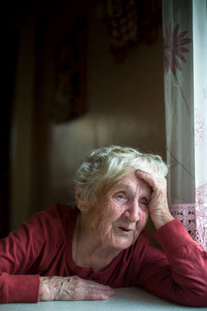 An emotional old lady is sitting at the kitchen table.