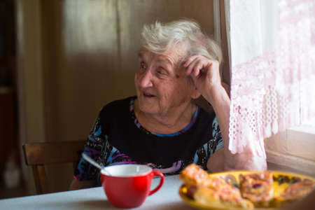 An elderly woman sitting at the table drinking tea with pies.の写真素材